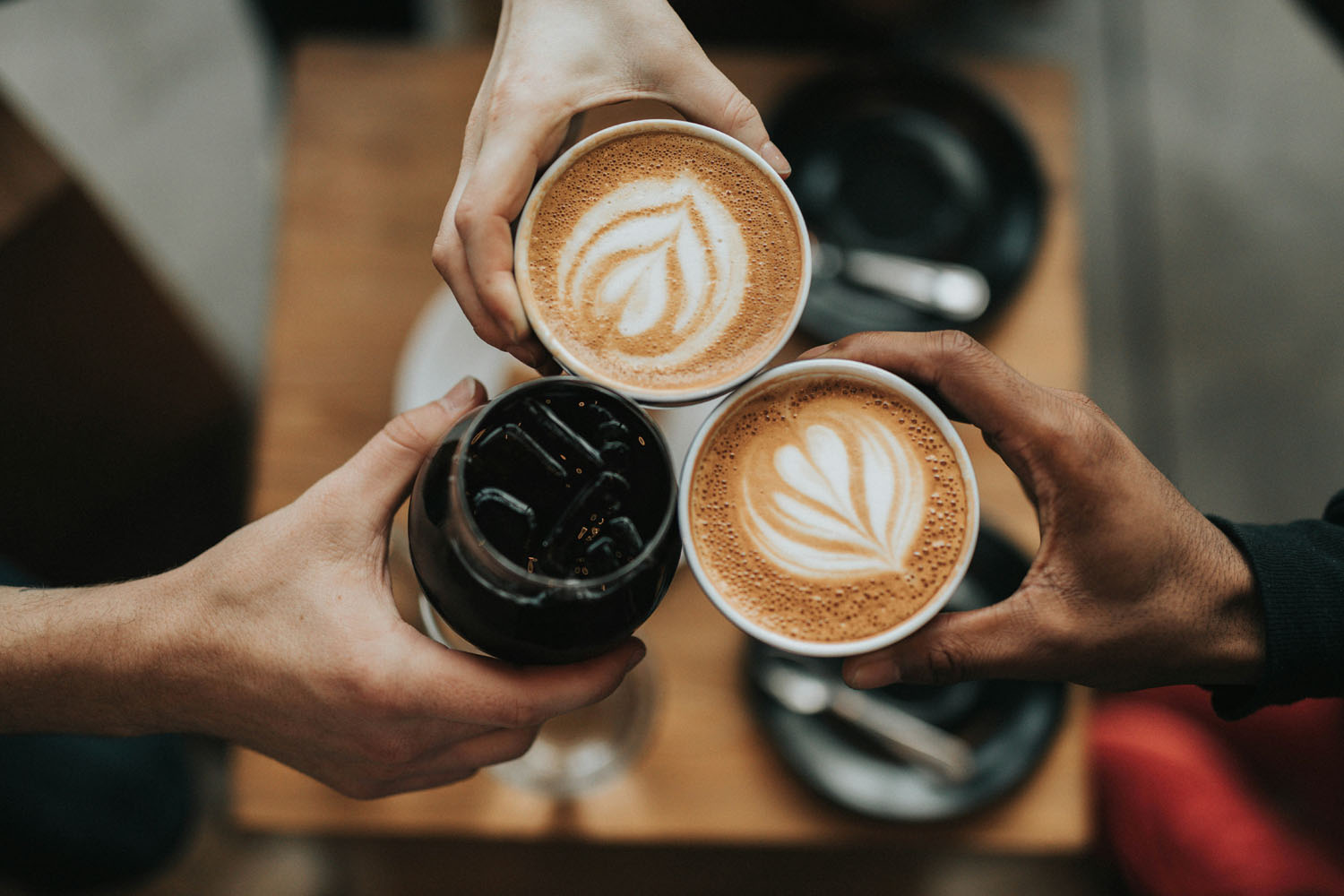 drie handen proosten met twee koffie en een cola